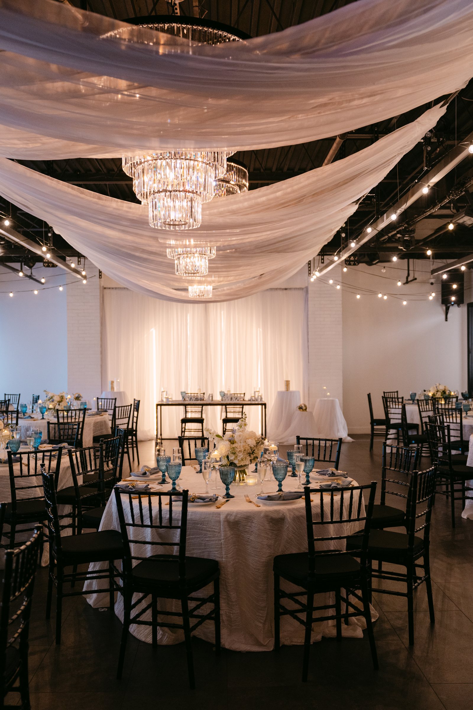 Reception tables beneath draped fabric and chandelier light at Trellis 925