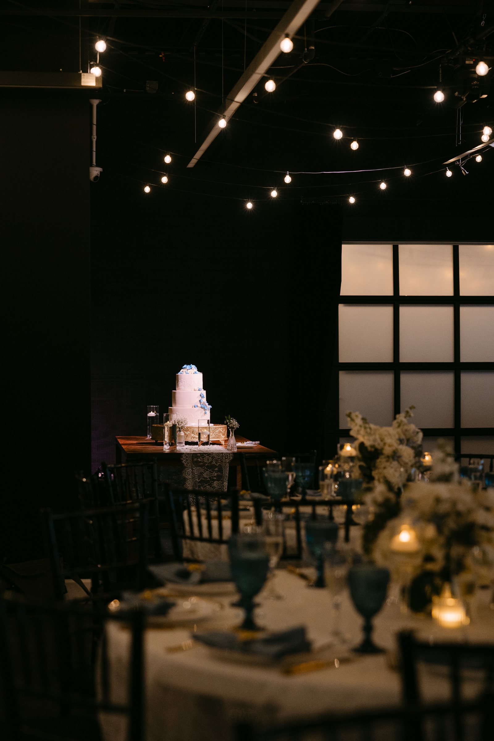 A wedding cake and reception tables in evening light at Trellis 925