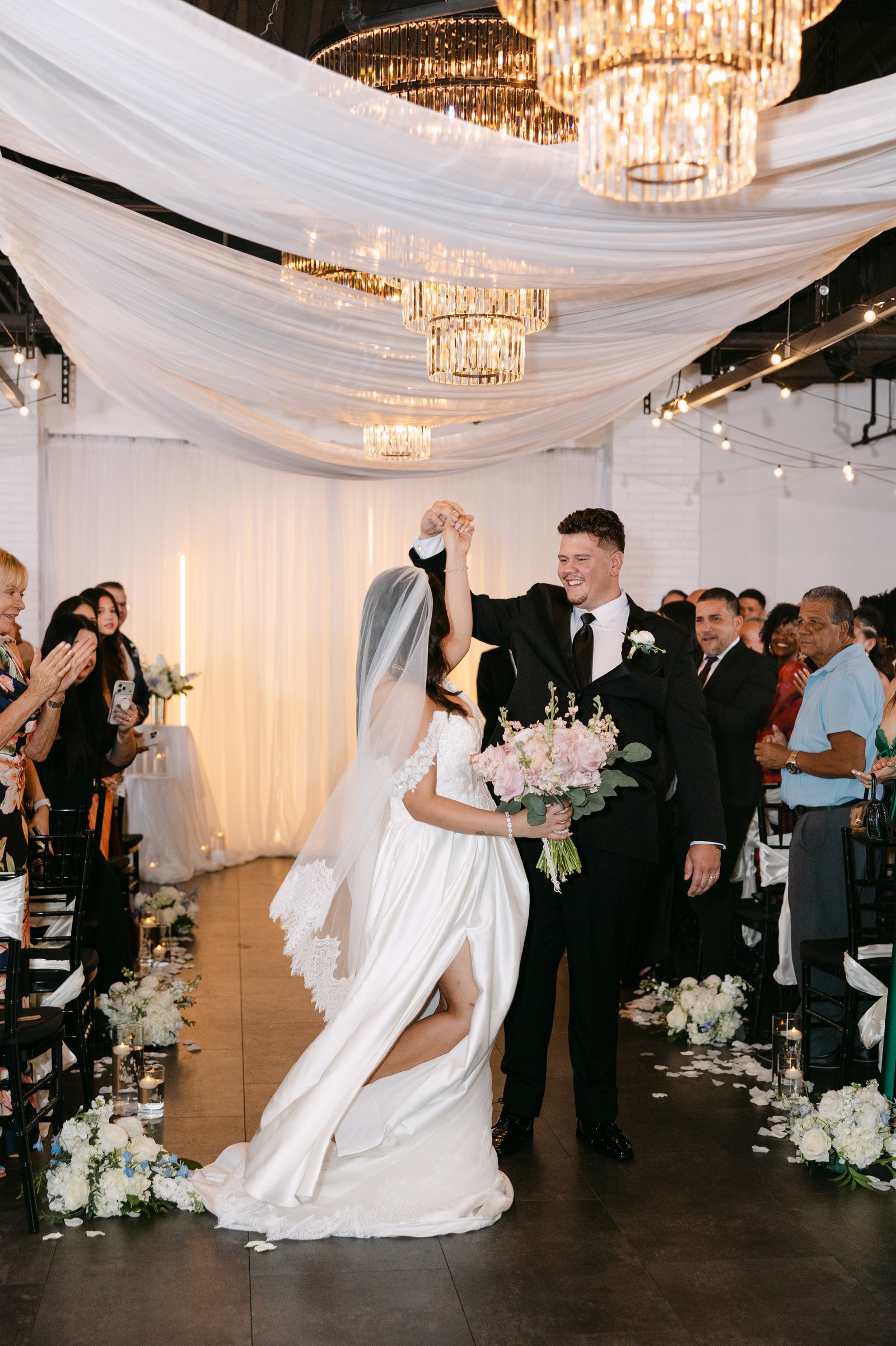 A wedding recessional beneath draped fabric and chandeliers at Trellis 925
